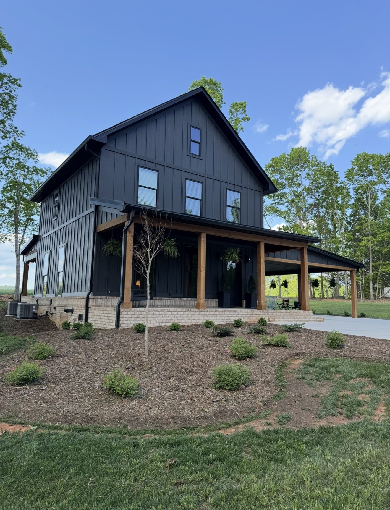 Completed two-story black farmhouse with timber porch and fresh landscaping