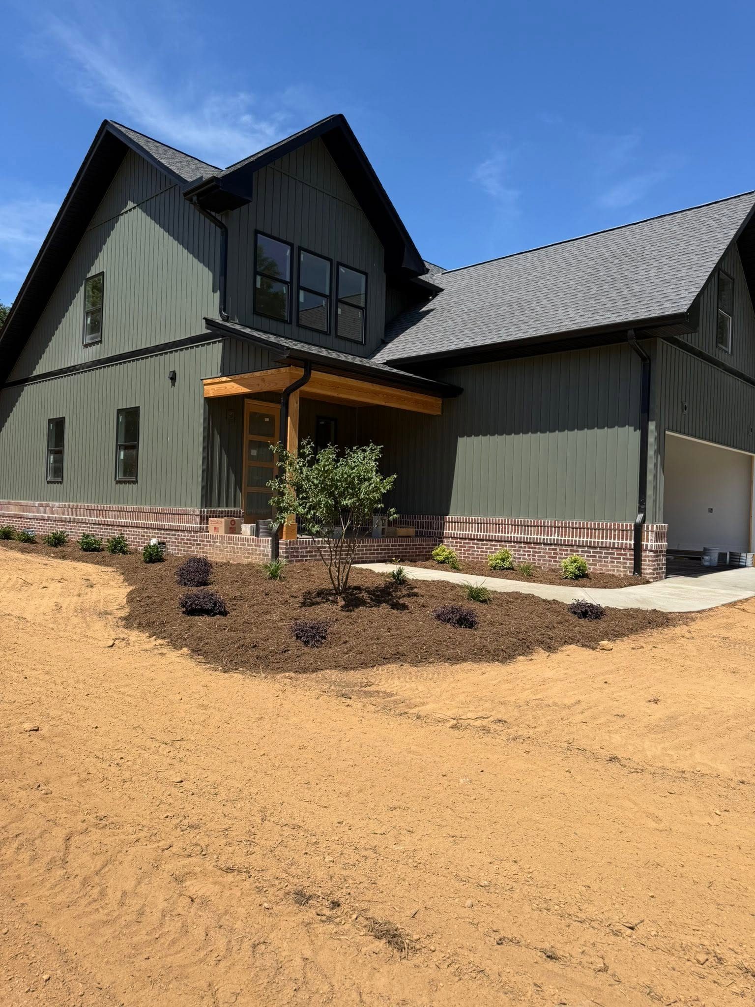 Completed green farmhouse with porch, brick skirt, and new landscaping over graded yard