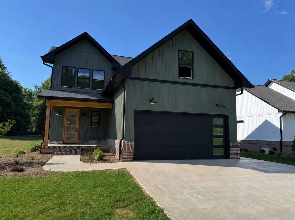 Completed two-story sage green farmhouse with dark garage and concrete driveway