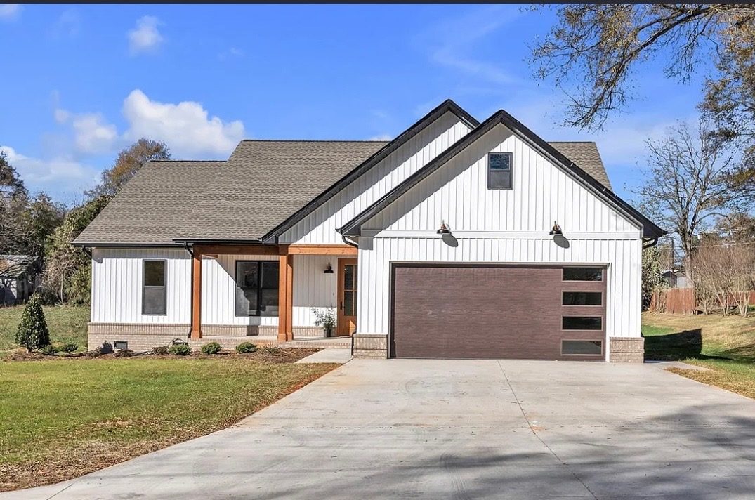 Completed white board-and-batten farmhouse with brick base, covered porch, and finished concrete drive